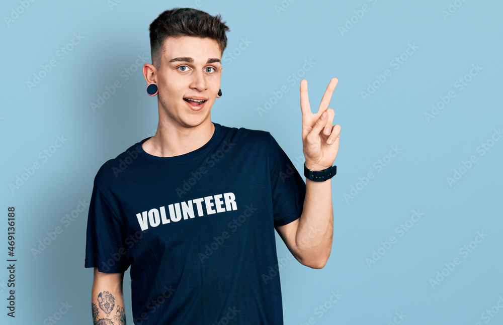 Young caucasian boy with ears dilation wearing volunteer t shirt smiling looking to the camera showing fingers doing victory sign. number two. Young caucasian boy with ears dilation wearing volunteer t shirt smiling looking to the camera showing fingers doing victory sign. number two.