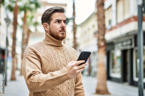 Young caucasian man with serious expression using smartphone at the city.