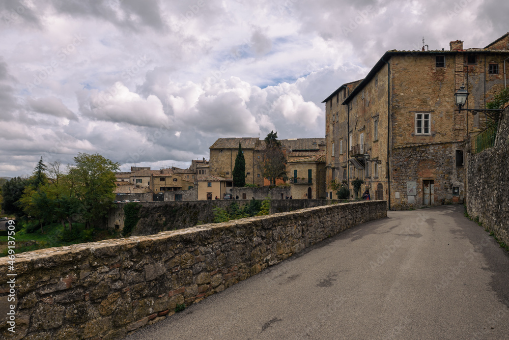 ausblick von Volterra auf die toskansiche Landscahft mit Himmel und Wolken und Gebäuden im Vordergrund und Straße mit Mauer