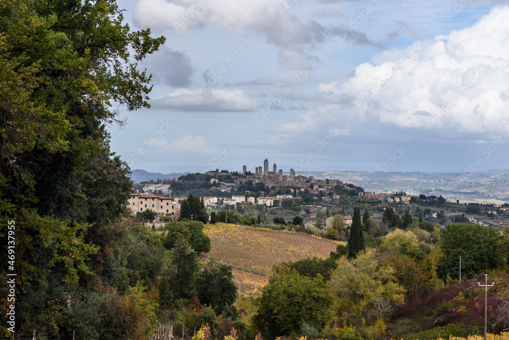 Blick über Weinberge in Herbstfarben und Bäume auf San Gimignano im Hintergrund in der Toskana