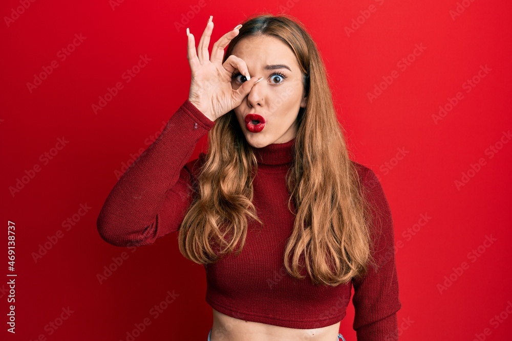 Young blonde woman wearing turtleneck sweater doing ok gesture shocked with surprised face, eye looking through fingers. unbelieving expression. Young blonde woman wearing turtleneck sweater doing ok gesture shocked with surprised face, eye looking through fingers. unbelieving expression.