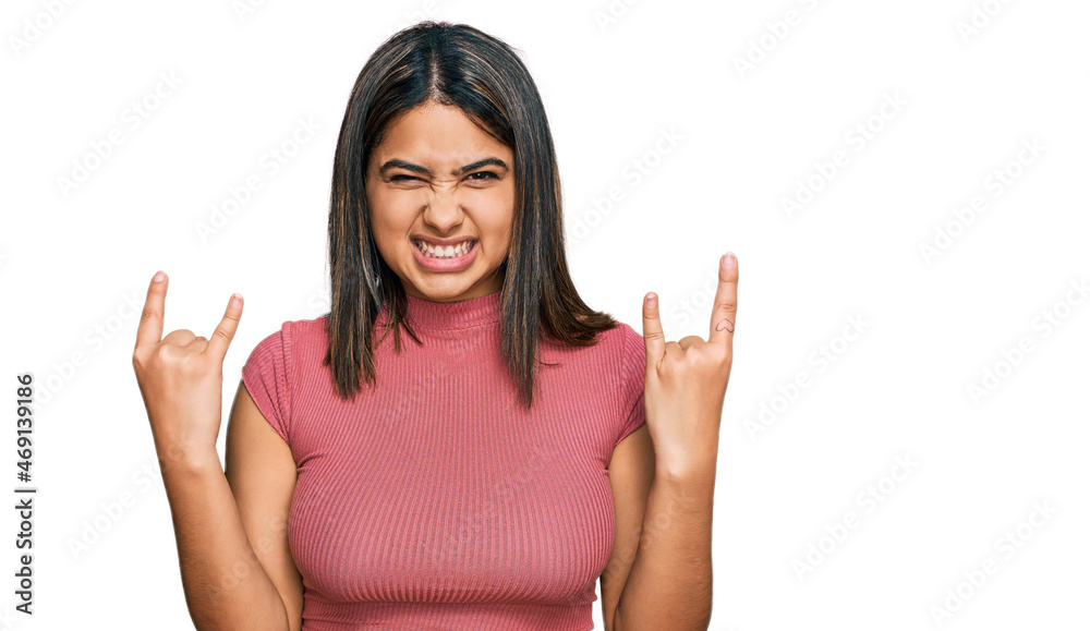 Young hispanic girl wearing casual t shirt shouting with crazy expression doing rock symbol with hands up. music star. heavy concept. Young hispanic girl wearing casual t shirt shouting with crazy expression doing rock symbol with hands up. music star. heavy concept.