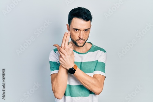 Young hispanic man wearing casual clothes holding symbolic gun with hand gesture, playing killing shooting weapons, angry face