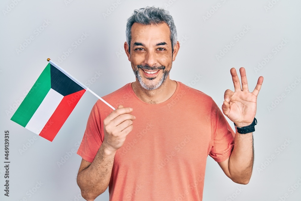 Handsome middle age man with grey hair holding kuwait flag doing ok sign with fingers, smiling friendly gesturing excellent symbol Handsome middle age man with grey hair holding kuwait flag doing ok sign with fingers, smiling friendly gesturing excellent symbol