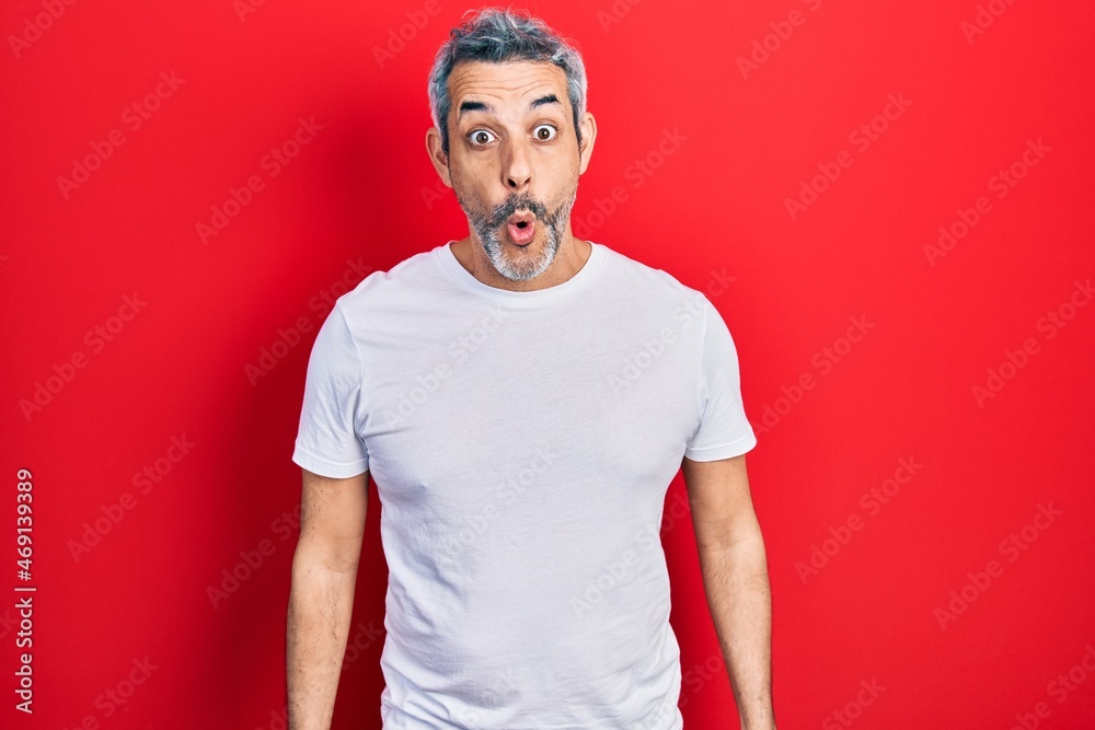Fototapeta premium Handsome middle age man with grey hair wearing casual white t shirt scared and amazed with open mouth for surprise, disbelief face