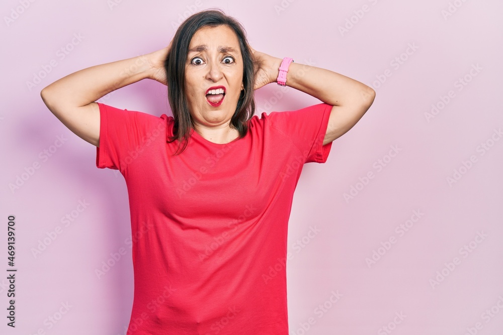 Middle age hispanic woman wearing casual clothes crazy and scared with hands on head, afraid and surprised of shock with open mouth Middle age hispanic woman wearing casual clothes crazy and scared with hands on head, afraid and surprised of shock with open mouth