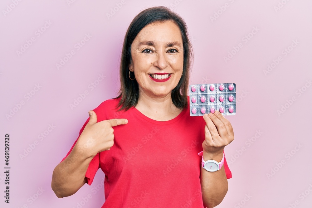 Middle age hispanic woman holding pills pointing finger to one self smiling happy and proud Middle age hispanic woman holding pills pointing finger to one self smiling happy and proud