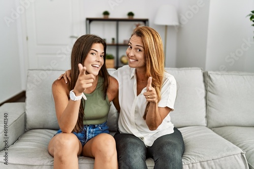Mother and daughter together sitting on the sofa at home pointing fingers to camera with happy and funny face. good energy and vibes.