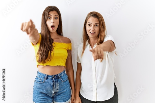 Mother and daughter together standing together over isolated background pointing with finger surprised ahead  open mouth amazed expression  something on the front