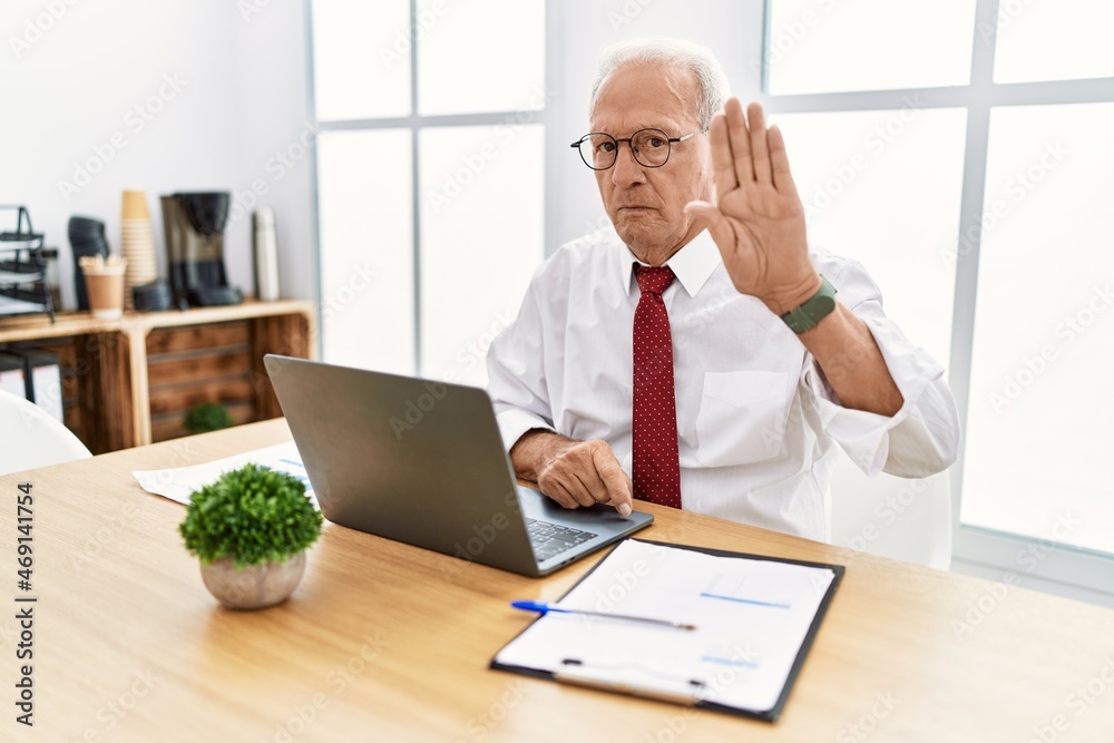 Senior man working at the office using computer laptop doing stop sing with palm of the hand. warning expression with negative and serious gesture on the face.