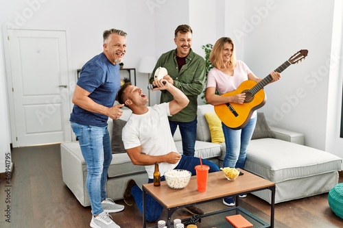 Group of middle age friends on party singing and playing guitar at home.