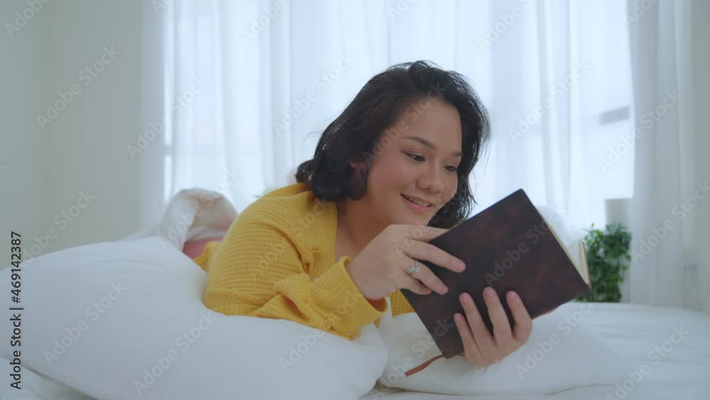 Asian woman oversize big chubby girl lying in bed. She wearing a yellow shirt reads books, novels, fairy tales, smiles and laughs happily. hobbies on holiday. Asian woman oversize big chubby girl lying in bed. She wearing a yellow shirt reads books, novels, fairy tales, smiles and laughs happily. hobbies on holiday.