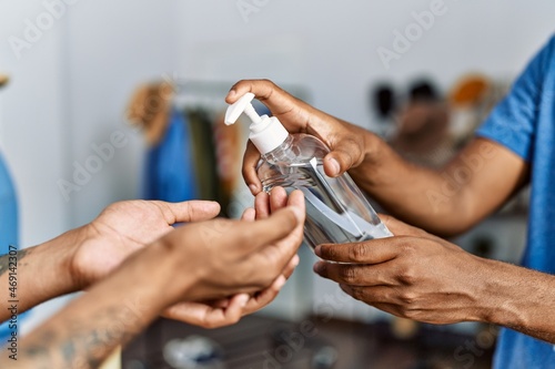Two men shopkeeper and customer cleaning hands using sanitizer gel at clothing store