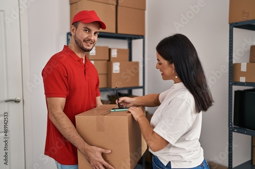 Man and woman deliveryman and worker holding package signing on smartphone at storehouse