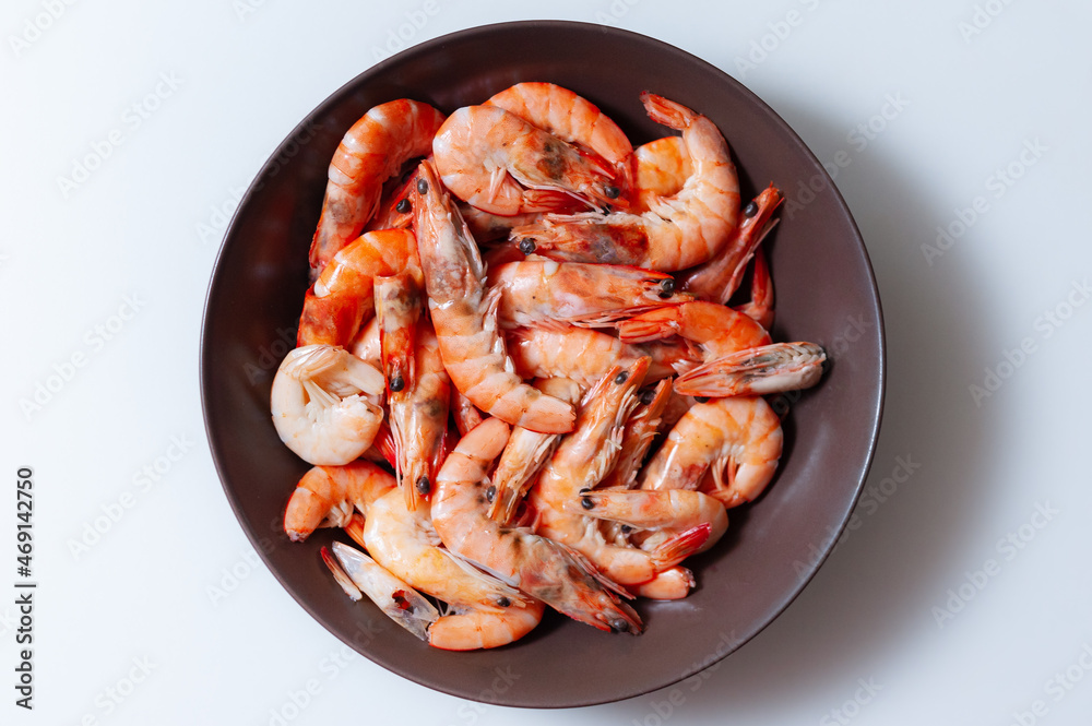 Unpeeled boiled shrimp in a dark plate on a white background