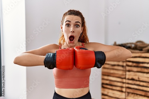 Young redhead woman using boxing gloves afraid and shocked with surprise and amazed expression, fear and excited face. © Krakenimages.com