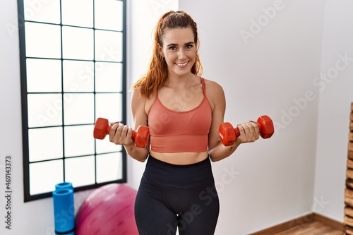 Young redhead woman smiling confident training with dumbbells at sport center
