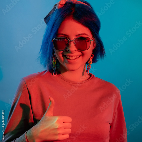 Approval gesture. Agree sign. Excellent idea. Red neon light joyful smiling woman showing thumbs up success symbol isolated on blue background.