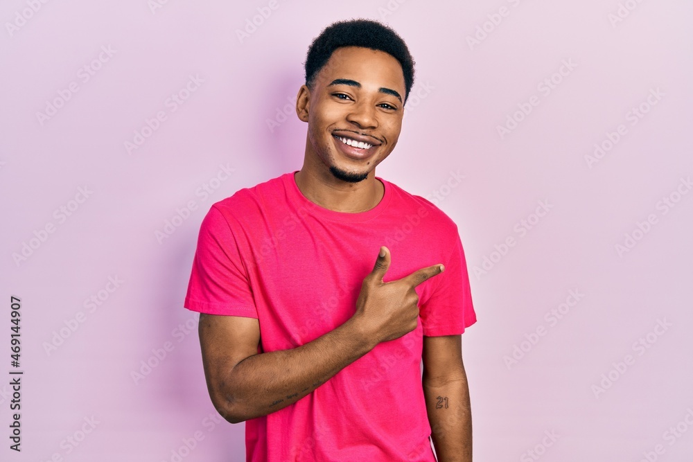 Young african american man wearing casua t shirt cheerful with a smile of face pointing with hand and finger up to the side with happy and natural expression on face Young african american man wearing casua t shirt cheerful with a smile of face pointing with hand and finger up to the side with happy and natural expression on face
