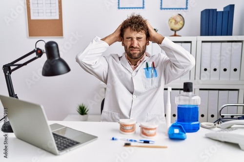 Fotografie Young hispanic dentist man working at medical clinic suffering from headache desperate and stressed because pain and migraine