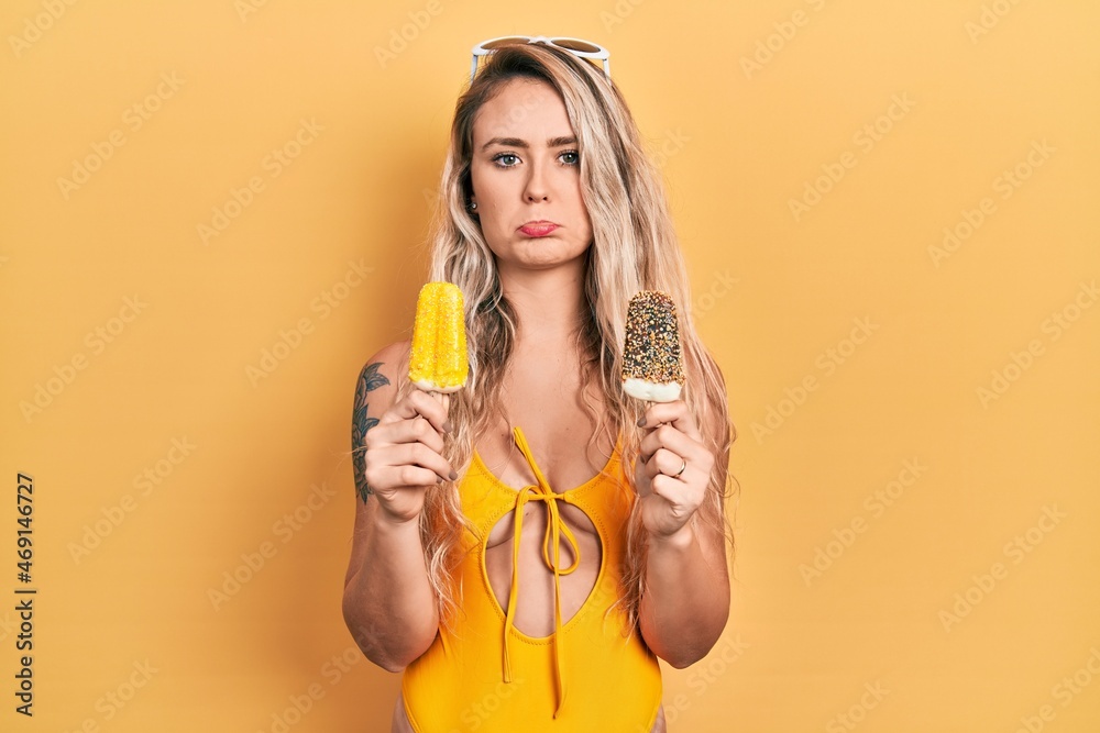 Beautiful young blonde woman wearing summer swimsuit holding ice creams depressed and worry for distress, crying angry and afraid. sad expression. Beautiful young blonde woman wearing summer swimsuit holding ice creams depressed and worry for distress, crying angry and afraid. sad expression.