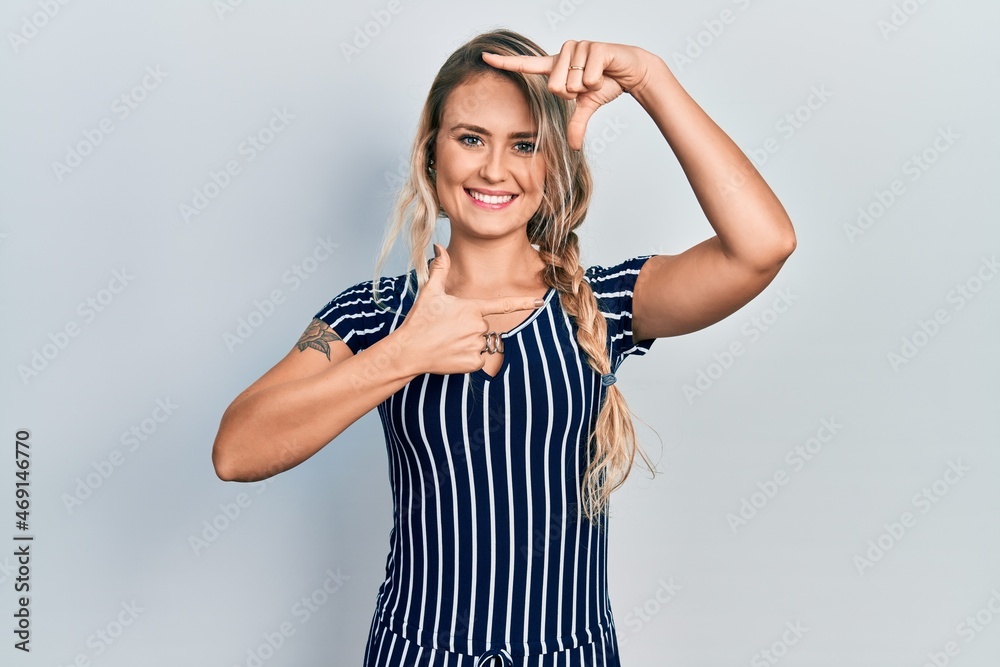 Beautiful young blonde woman wearing casual striped dress smiling making frame with hands and fingers with happy face. creativity and photography concept. Beautiful young blonde woman wearing casual striped dress smiling making frame with hands and fingers with happy face. creativity and photography concept.