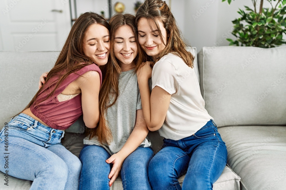 Three young hispanic woman smiling happy and hugging sitting on the sofa at home.