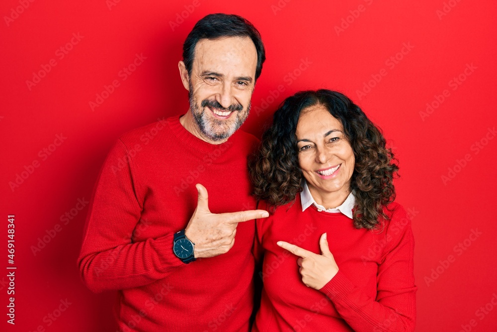 Middle age couple of hispanic woman and man hugging and standing together cheerful with a smile on face pointing with hand and finger up to the side with happy and natural expression Middle age couple of hispanic woman and man hugging and standing together cheerful with a smile on face pointing with hand and finger up to the side with happy and natural expression