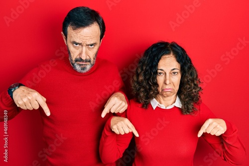 Middle age couple of hispanic woman and man hugging and standing together pointing down looking sad and upset, indicating direction with fingers, unhappy and depressed. © Krakenimages.com