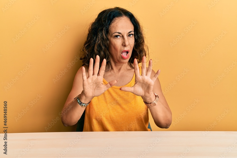 Beautiful middle age woman wearing casual clothes sitting on the table doing stop gesture with hands palms, angry and frustration expression Beautiful middle age woman wearing casual clothes sitting on the table doing stop gesture with hands palms, angry and frustration expression