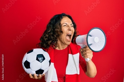 Middle age hispanic woman hooligan screaming through megaphone supporting soccer team photo