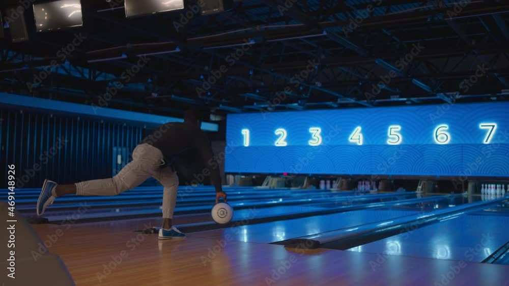 A black man bowling man throws a ball in slow motion and knocks down