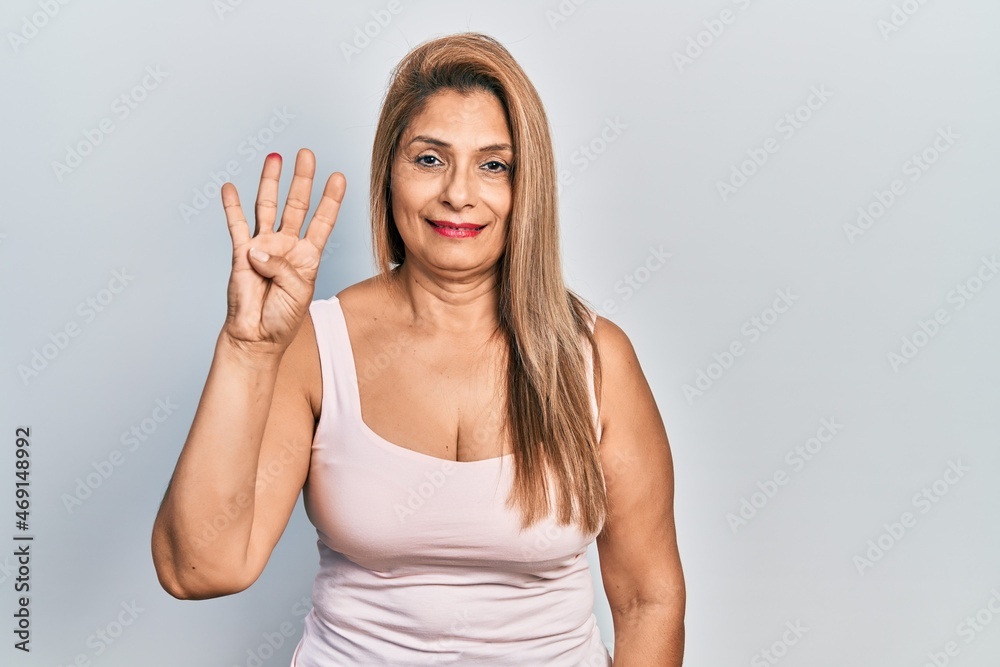 Middle age hispanic woman wearing casual style with sleeveless shirt showing and pointing up with fingers number four while smiling confident and happy. Middle age hispanic woman wearing casual style with sleeveless shirt showing and pointing up with fingers number four while smiling confident and happy.