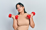 Young hispanic woman wearing sportswear using dumbbells looking at the camera blowing a kiss being lovely and sexy. love expression.