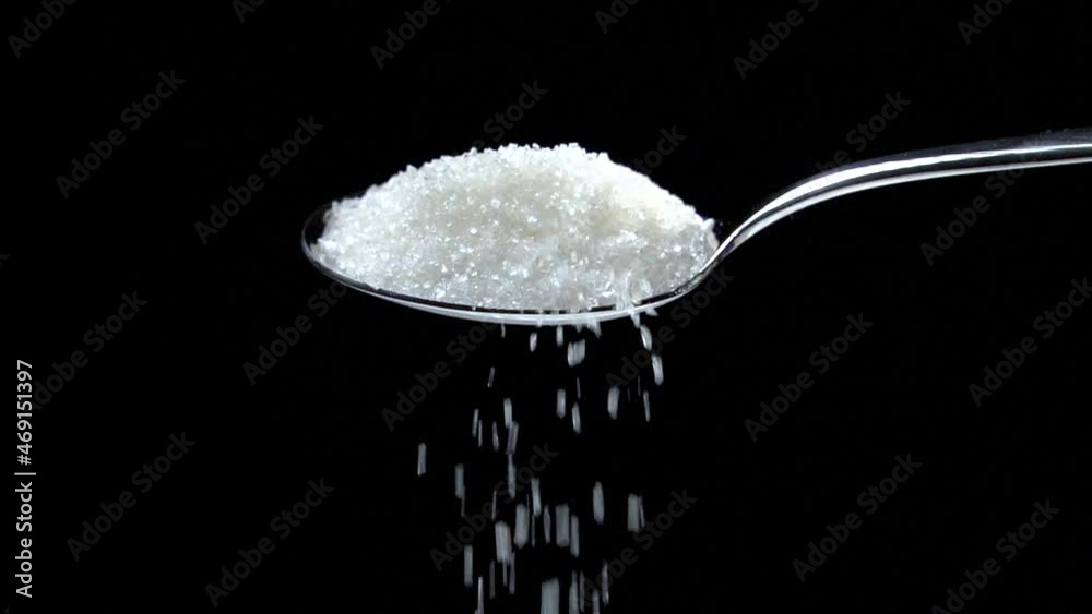 Sugar falling from spoon in slow motion on black background