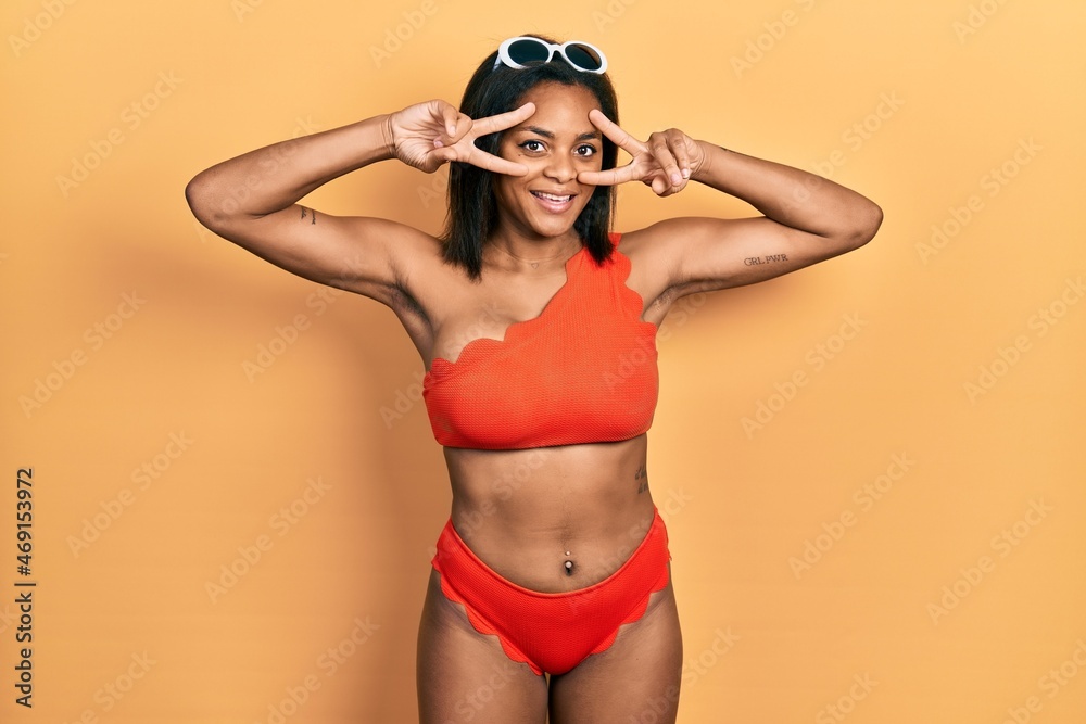 Young african american girl wearing bikini doing peace symbol with fingers over face, smiling cheerful showing victory Young african american girl wearing bikini doing peace symbol with fingers over face, smiling cheerful showing victory