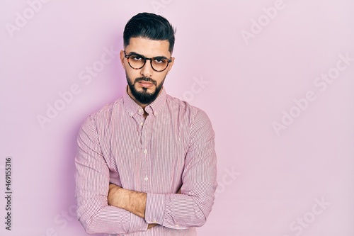 Handsome man with beard wearing casual shirt and glasses skeptic and nervous, disapproving expression on face with crossed arms. negative person.