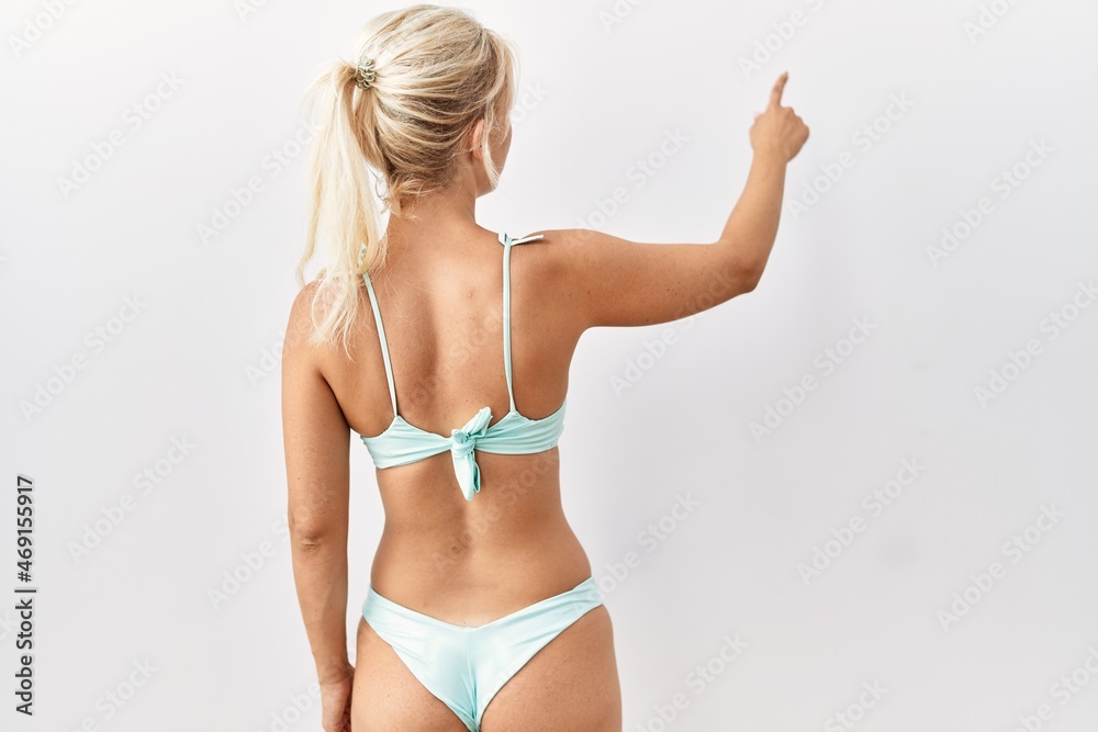 Young caucasian woman wearing bikini over isolated background posing backwards pointing ahead with finger hand Young caucasian woman wearing bikini over isolated background posing backwards pointing ahead with finger hand