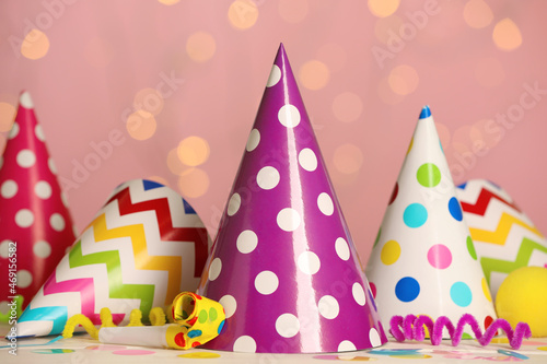 Fototapeta Naklejka Na Ścianę i Meble -  Colorful party hats and festive items on white table against pink background with blurred lights