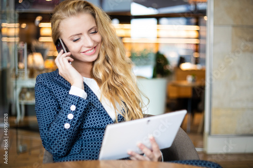 Portrait of a young woman talking on the phone and using a digital tablet on a break