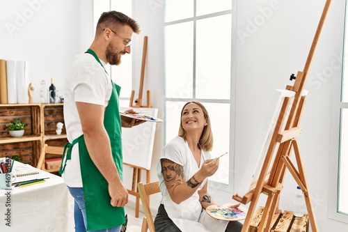 Young caucasian couple smiling happy drawing at art studio. Man standing and looking draw canvas.