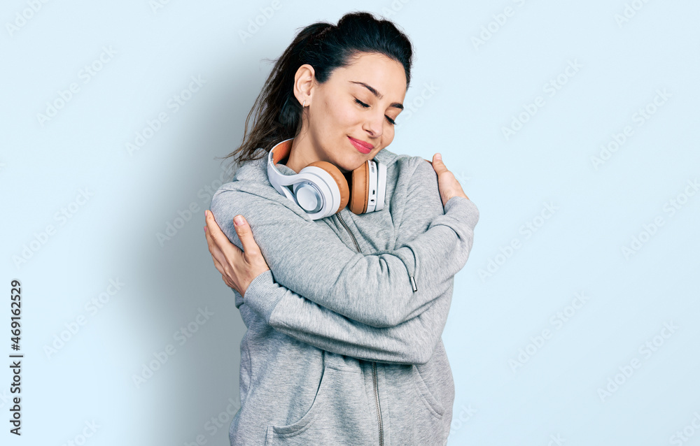 Young hispanic woman wearing gym clothes and using headphones hugging oneself happy and positive, smiling confident. self love and self care Young hispanic woman wearing gym clothes and using headphones hugging oneself happy and positive, smiling confident. self love and self care
