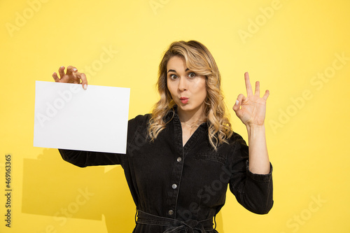 Valokuva young beautiful blonde woman in black dress holds empty sheet for inscription on