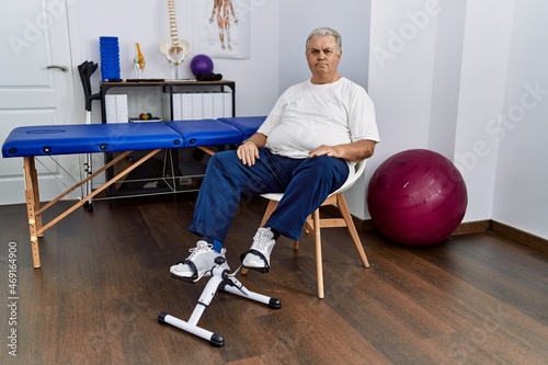 Senior caucasian man at physiotherapy clinic using pedal exerciser relaxed with serious expression on face. simple and natural looking at the camera.