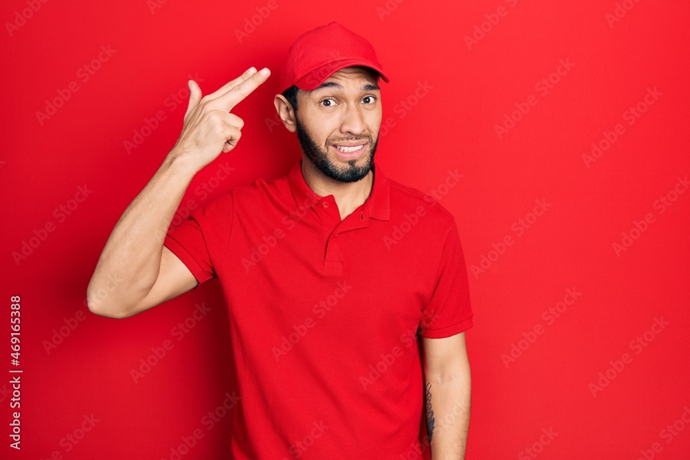 Hispanic man with beard wearing delivery uniform and cap shooting and killing oneself pointing hand and fingers to head like gun, suicide gesture. Hispanic man with beard wearing delivery uniform and cap shooting and killing oneself pointing hand and fingers to head like gun, suicide gesture.