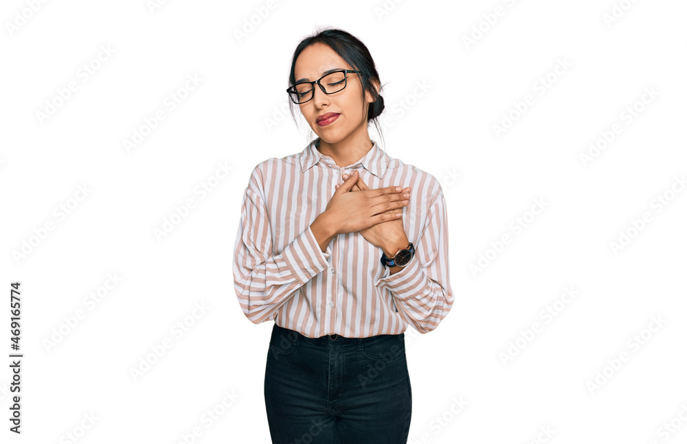 Young hispanic girl wearing casual clothes and glasses smiling with hands on chest with closed eyes and grateful gesture on face. health concept. Young hispanic girl wearing casual clothes and glasses smiling with hands on chest with closed eyes and grateful gesture on face. health concept.