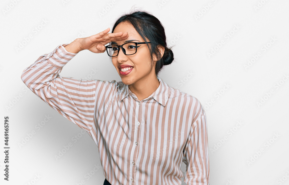 Young hispanic girl wearing casual clothes and glasses very happy and smiling looking far away with hand over head. searching concept. Young hispanic girl wearing casual clothes and glasses very happy and smiling looking far away with hand over head. searching concept.