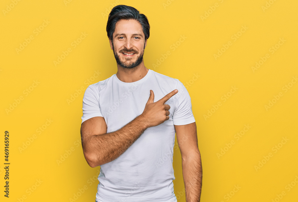 Young hispanic man wearing casual white t shirt cheerful with a smile of face pointing with hand and finger up to the side with happy and natural expression on face Young hispanic man wearing casual white t shirt cheerful with a smile of face pointing with hand and finger up to the side with happy and natural expression on face