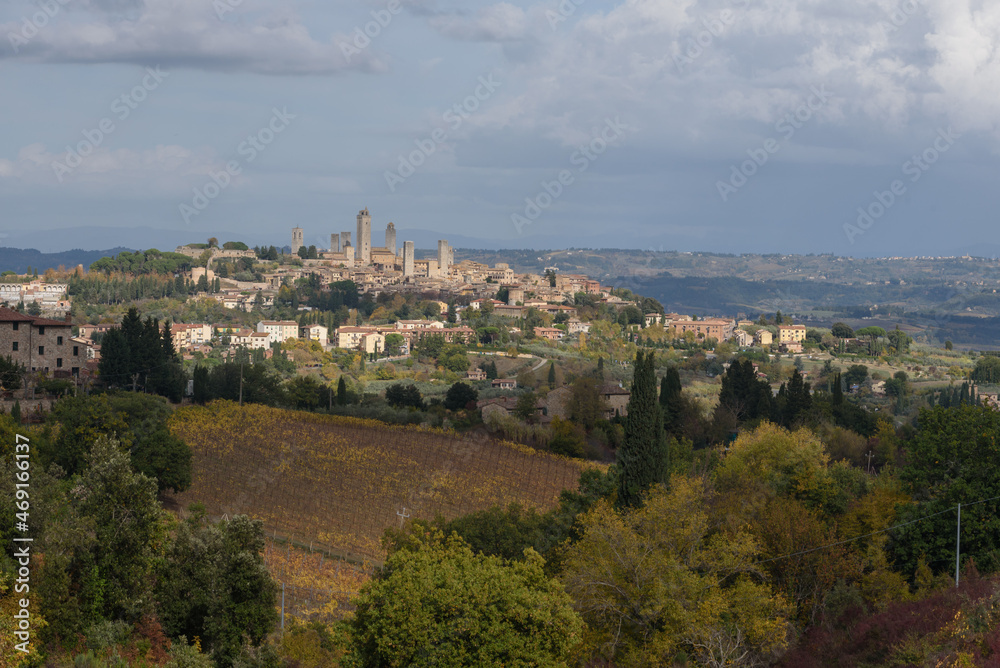 Blick über Weinberge in Herbstfarben und Bäume auf San Gimignano im Hintergrund in der Toskana