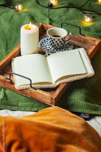 Cup of coffee and notebook with candle in tray in bed